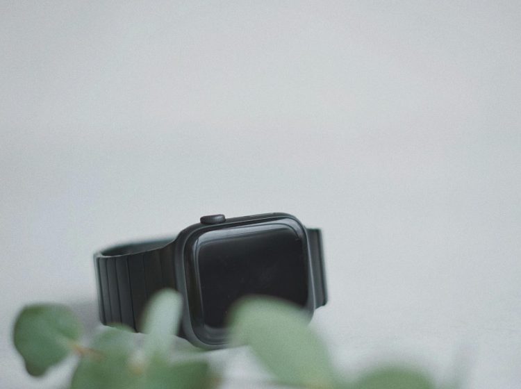 Sleek black smartwatch on a white background with green leaves, showcasing modern technology.